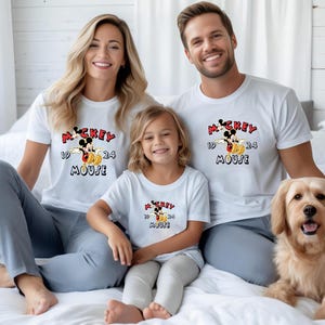 May include: A family and a dog are sitting on a bed, all wearing matching white t-shirts. The shirts feature a Mickey Mouse graphic with the words "Mickey Mouse" and the numbers "1924". The dog is a golden retriever.