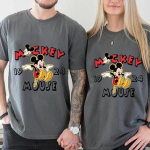 May include: Two grey t-shirts with a Mickey Mouse graphic. The design includes the word "Mickey" in red, the year "1924", and the word "Mouse" in black. The shirts are short-sleeved.