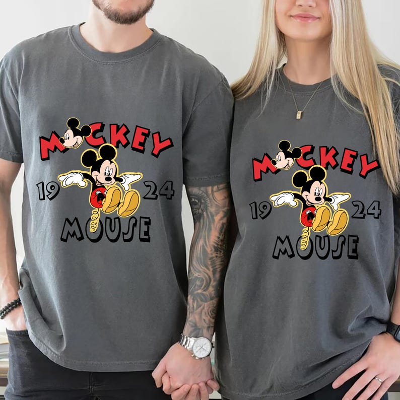 May include: Two grey t-shirts with a Mickey Mouse graphic. The design includes the word "Mickey" in red, the year "1924", and the word "Mouse" in black. The shirts are short-sleeved.