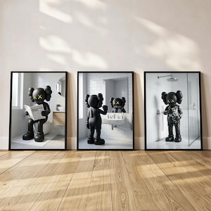 May include: Set of three framed art prints featuring a black cartoon figure in bathroom scenes. The figure is depicted in a bathroom, brushing its teeth, and taking a shower. The figure has yellow cross-shaped eyes.
