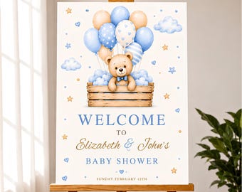 May include: A rectangular welcome sign for a baby shower featuring a teddy bear in a wooden crate attached to blue and beige balloons. The text reads: WELCOME TO Elizabeth & John's BABY SHOWER SUNDAY FEBRUARY 12TH. The design includes clouds and stars.