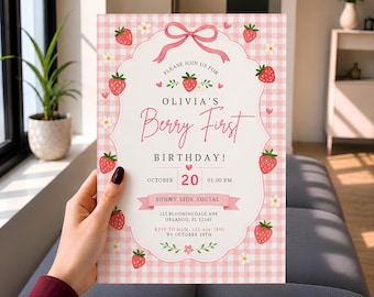 May include: A rectangular birthday invitation card featuring a pink and white gingham background with strawberry and white flower illustrations. The center includes a scalloped white frame with a pink bow and text reading Olivia's Berry First Birthday.