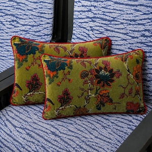 May include: Two rectangular throw pillows featuring a moss green velvet base with a multi-colored floral pattern in shades of dark blue, orange, and deep red. Each pillow is finished with a thin, solid red piping along the outer edges.