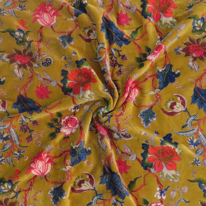 Puede incluir: Una tela de terciopelo color amarillo mostaza con un patr&oacute;n floral repetitivo de grandes rosas rojas, flores rosadas m&aacute;s peque&ntilde;as y enredaderas de hojas azul oscuro. El tejido tiene una textura suave y reflectante con un estampado bot&aacute;nico denso.