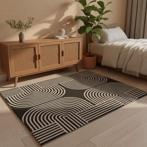 Può includere: Un tappeto a motivi geometrici in bianco e nero con un motivo ad arco ripetuto. Il tappeto è rettangolare e si trova su un pavimento in legno chiaro. Un mobile in legno e una struttura letto sono visibili sullo sfondo.