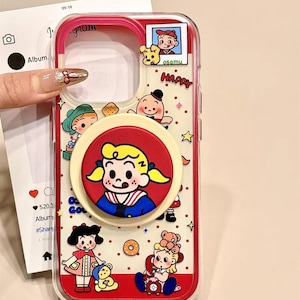 May include: A clear phone case with a red border featuring cartoon characters and the text "HAPPY". The case has a pop-up grip with a cartoon girl design. The bottom right corner has the text "ASSxCase".