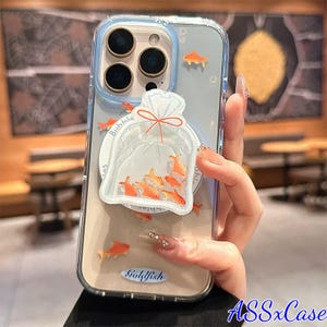May include: Clear phone case with a goldfish theme. The case features a bag of goldfish design and several orange fish accents. The case has a blue border and the text "Goldfish" is at the bottom. The brand name "ASSxCase" is visible.