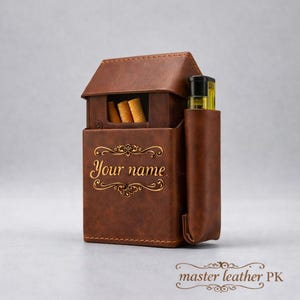 Puede incluir: Un estuche de cigarrillos de cuero marrón con un soporte para encendedor. El estuche tiene las palabras "Your name" en letras doradas y un diseño decorativo. También es visible la marca "master leather PK".