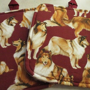 May include: Two red pot holders with a pattern of brown and white Collie dogs. The pot holders have a loop for hanging.