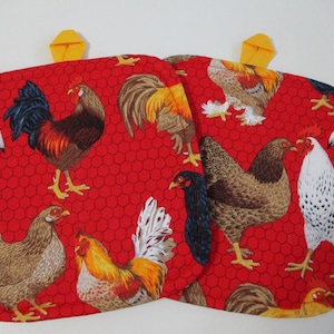 May include: Two red oven mitts with a repeating pattern of chickens and roosters in various colors. The mitts have yellow loops for hanging.