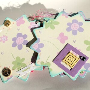 May include: A multi-layered scrapbook page with a light blue, white, and pink floral design. The page has a purple frame with the letter "B" inside. The page also has several white banners with the words "sweetest", "snuggle", and "angel" written on them.