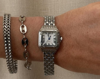 Relógio retangular prateado com data em algarismos romanos e mecanismo de quartzo.