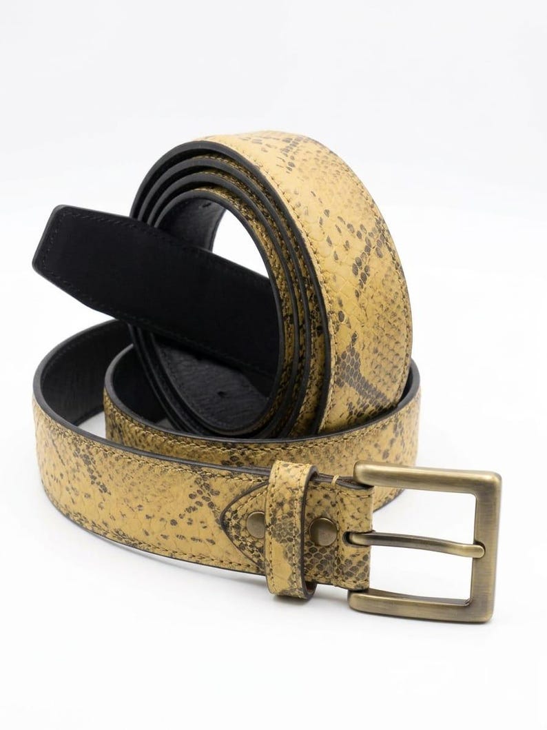 K&ouml;nnte beinhalten: Ein aufgerollter G&uuml;rtel mit Schlangenmuster in Beige- und Braunt&ouml;nen. Der G&uuml;rtel hat eine schwarze Innenseite und eine rechteckige, antik-messingfarbene Schnalle. Der G&uuml;rtel ist aus Leder.