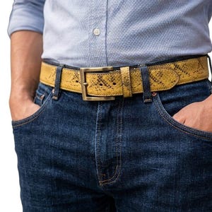 K&ouml;nnte beinhalten: Ein gelber G&uuml;rtel mit Schlangenmuster und einer rechteckigen Messingschnalle. Der G&uuml;rtel wird mit einer blauen Jeans und einem hellblauen Hemd getragen. Die Breite des G&uuml;rtels betr&auml;gt ca. 3,8 cm.