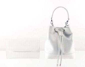 May include: A white bucket bag with a drawstring closure and a top handle. The bag is made from a textured leather-like material.