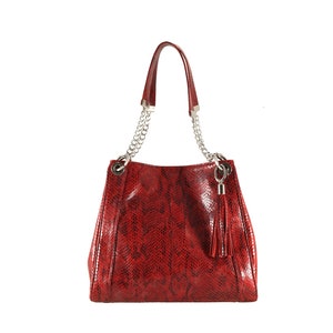 Puede incluir: Un bolso de mano de cuero rojo con estampado de serpiente, con una correa de cadena plateada y un borla.