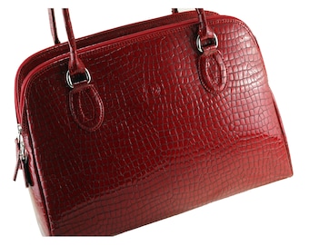 Könnte beinhalten: Eine rote, glänzende Handtasche mit Krokodilleder-Textur. Die Tasche hat zwei Griffe, einen Reißverschluss und silberfarbene Beschläge. Die Tasche hat einen tiefen Rotton.