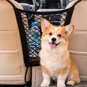 May include: A happy corgi dog sits in a car, next to a black mesh organizer with a water bottle. The dog has orange and white fur and is smiling with its tongue out. The car interior is beige.