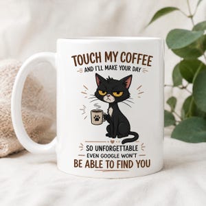 Puede incluir: Taza de cerámica blanca con un gato negro gruñón sosteniendo una taza de café. La taza tiene el texto "TOUCH MY COFFEE AND I'LL MAKE YOUR DAY" y "SO UNFORGETTABLE - EVEN GOOGLE WON'T BE ABLE TO FIND YOU."