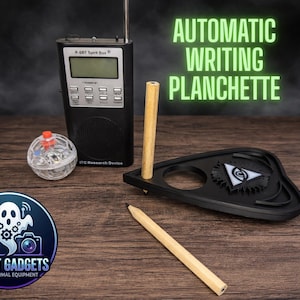 May include: A black P-SB7 Spirit Box radio, a clear orb with a red top, a black planchette with an eye symbol, two wooden dowels, and a pencil are arranged on a wooden surface. The text "AUTOMATIC WRITING PLANCHETTE" is displayed in green. A logo for "Ghost Gadgets" is in the lower left.