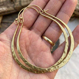 May include: A pair of large, teardrop-shaped hoop earrings crafted from hammered gold-tone metal. Each earring features a textured, dimpled surface and a simple wire closure mechanism with a small ball detail at the top of the hoop structure.