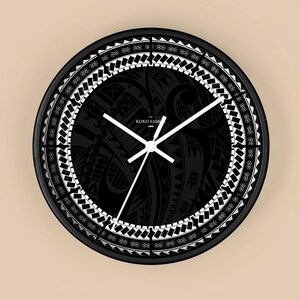 May include: A round black wall clock with white hands and a black face featuring a white geometric border. The clock face has a black tribal design with the text "KOKO SAMOA".