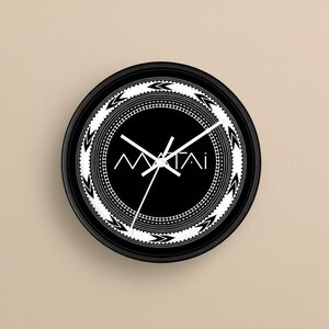 May include: A round black wall clock with white hands and a black face. The clock face features the word "MAITAI" in white, surrounded by a white decorative border. The clock is approximately 10 inches in diameter.