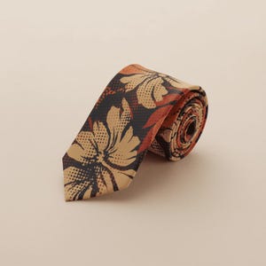 May include: A necktie featuring a dark brown background with a repeating floral pattern in tan and burnt orange. The design incorporates a halftone dot texture throughout the petals and leaves, creating a layered visual effect on the fabric.