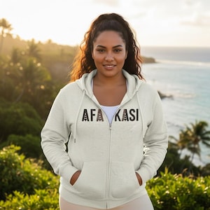 May include: A light heather gray zip-up hoodie featuring a hood with matching drawstrings, long sleeves, and two front pockets. The text AFA KASI is printed across the chest in a dark, patterned font with a repeating geometric design.