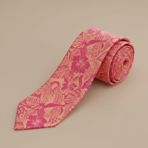 Puede incluir: Una corbata con un vibrante estampado floral y de hojas tropicales en color rosa intenso sobre un fondo color melocotón claro. La corbata está enrollada en un extremo y muestra una punta en el otro, con un diseño botánico constante.