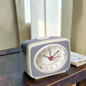 Puede incluir: Una taza de cerámica blanca con un asa negra y el texto "But First, Coffee" en negro y negrita. La taza está sobre una superficie blanca. La taza mide aproximadamente 10 cm de alto.