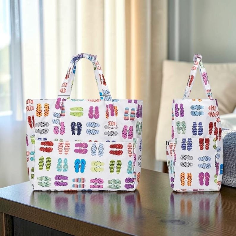 Może przedstawiać: Dwie białe torby typu tote z kolorowym wzorem klapek. Torby mają r&oacute;żne wzory klapek w odcieniach niebieskiego, zielonego, r&oacute;żowego, pomarańczowego i fioletowego. Leżą na ciemnej drewnianej powierzchni.