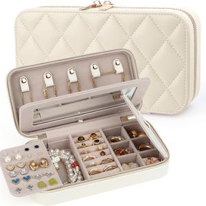 May include: A cream-colored, quilted rectangular jewelry organizer case with a zipper closure. The interior features a mirror, necklace hooks, a removable earring panel, and multiple compartments for rings and bracelets, all lined in a soft fabric.