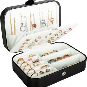 May include: A black rectangular jewelry box with a white interior. The lid features hooks for necklaces and a panel for earrings. The base contains multiple compartments with slots for rings and open sections for various pieces of jewelry.
