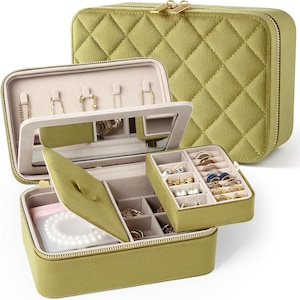 May include: Olive green jewelry organizer with a quilted exterior and gold zipper. The interior features compartments for rings, necklaces, and earrings, along with a mirror. The organizer is designed to keep jewelry safe and organized.