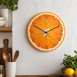 Puede incluir: Un reloj de pared redondo con diseño de rodaja de naranja. La esfera del reloj presenta una textura de naranja realista con números y manecillas negras. El reloj está montado en una pared blanca, ideal para la cocina o el comedor. Mide unos 25 cm de diámetro.