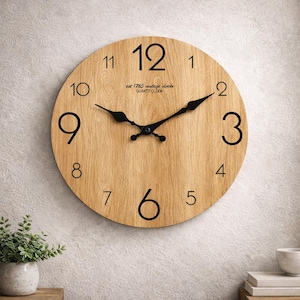 Op de afbeelding: Een ronde houten wandklok met zwarte cijfers en wijzers. De wijzerplaat heeft een licht houtnerfpatroon. De tekst "est 1765 vintage clocks QUARTZ CLOCK" is in het midden gedrukt.