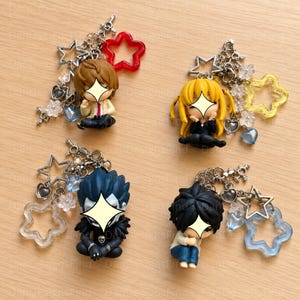 May include: Four anime-style character keychains featuring chibi figures with star-shaped charms. The figures include a brown-haired character, a blonde character, a dark-haired creature, and a black-haired character, all with metal chains and star accents.
