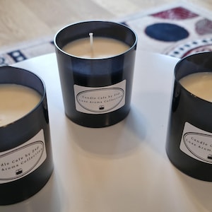 Può includere: Tre candele cilindriche in vetro nero con cera bianca e uno stoppino centrale. Ogni candela presenta un'etichetta ovale bianca con il testo nero Candle Cafe by Z&P Luxe Aroma Collection e una piccola icona di una candela.