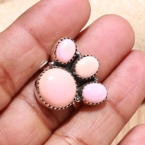 Könnte beinhalten: Ein Ring aus Sterlingsilber mit vier glatten, im Cabochon-Schliff gearbeiteten rosa Steinen unterschiedlicher Größe, die in einer Gruppe angeordnet sind. Der größte runde Stein befindet sich links, daneben drei kleinere ovale Steine.
