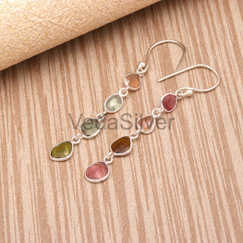 The sterling silver earrings with faceted multi-color tourmaline stones laid out on a wooden surface.