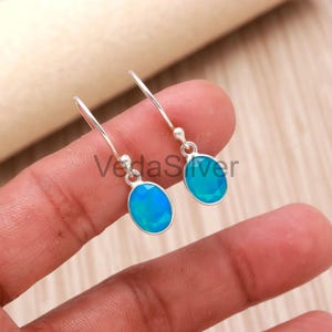 May include: A pair of silver drop earrings with oval, light blue opal stones. The earrings have a simple design with a hook closure. The gemstones are a vibrant, eye-catching color.