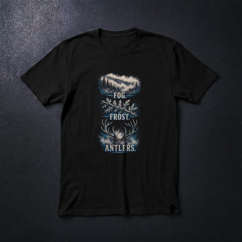 Pu&ograve; includere: T-shirt nera con un design a tema natura. Il design include illustrazioni di una scena di montagna, un ramo ghiacciato e corna di cervo, con le parole "FOG. FROST. ANTLERS." in un font stilizzato. L'opera d'arte &egrave; in tonalit&agrave; di blu e bianco.