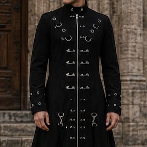 May include: A long black coat with a high collar and silver metal detailing. The coat has metal rings and clasps down the front and on the sleeves. It has a long, flowing skirt and is worn with black boots. The coat is a gothic style, suitable for cosplay or alternative fashion.