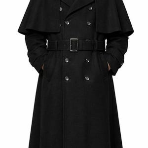 May include: A long, black wool coat with a capelet, double-breasted front, and a belt. The coat features a velvet collar and multiple buttons. The person is wearing a black shirt and tie. The coat is a classic style.