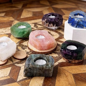 Puede incluir: Una colección de candelabros de piedras preciosas en varios colores, incluyendo verde, rosa, morado, azul y blanco. Cada uno tiene una hendidura circular para sostener una pequeña vela blanca. Algunos están sobre posavasos de madera.