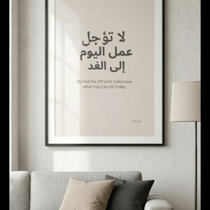 Può includere: Opera d'arte da parete incorniciata con testo arabo e traduzione inglese: "Non rimandare a domani quello che puoi fare oggi". L'opera è in una cornice nera, sopra un divano grigio con cuscini decorativi. La stanza ha una palette di colori neutri.
