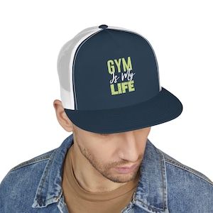 Puede incluir: Gorra de camionero azul marino con parte trasera de malla blanca. La gorra tiene el texto "GYM Is My LIFE" en verde claro. Tiene una visera plana y cierre snapback.