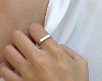 Könnte beinhalten: Ein goldener, rechteckiger Bandring, der an einem Finger getragen wird.