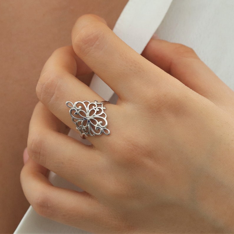 K&ouml;nnte beinhalten: Ein silberner Filigranring mit einem zarten, filigranen Design. Der Ring ist quadratisch und hat ein florales Muster.